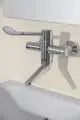Wandthermostat in Chrom mit Hebel und zwei Anschlüssen, montiert an einer hellen Wand, von der Marke Ideal Standard.